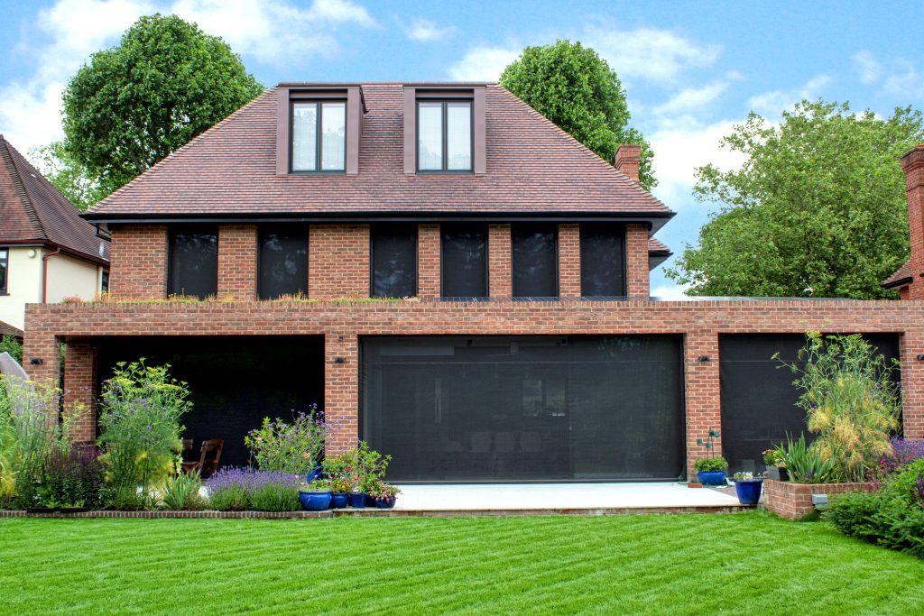 A large red bricked house with automated solar screens on a hot day